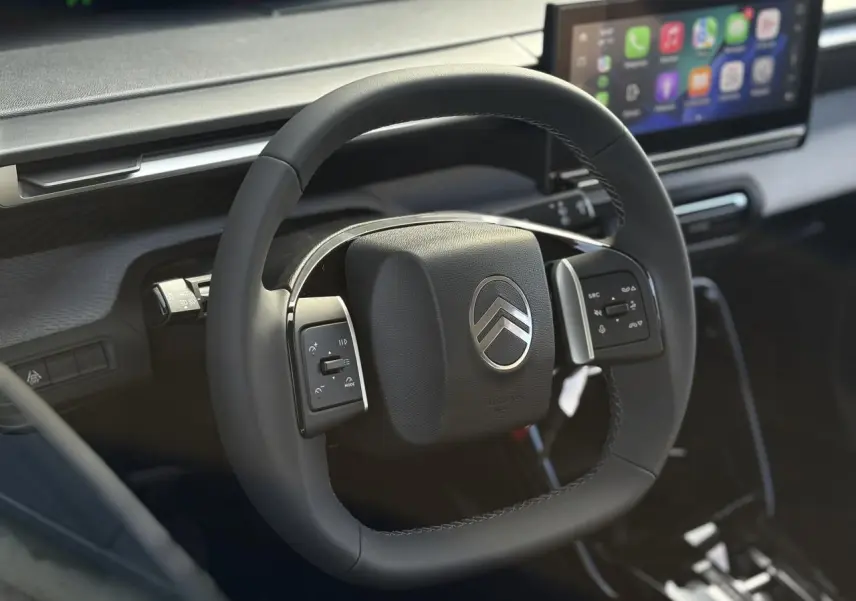 Gros plan sur le volant multifonctions carré noir du Citroën C3 Aircross 2025 avec écran tactile en arrière-plan.