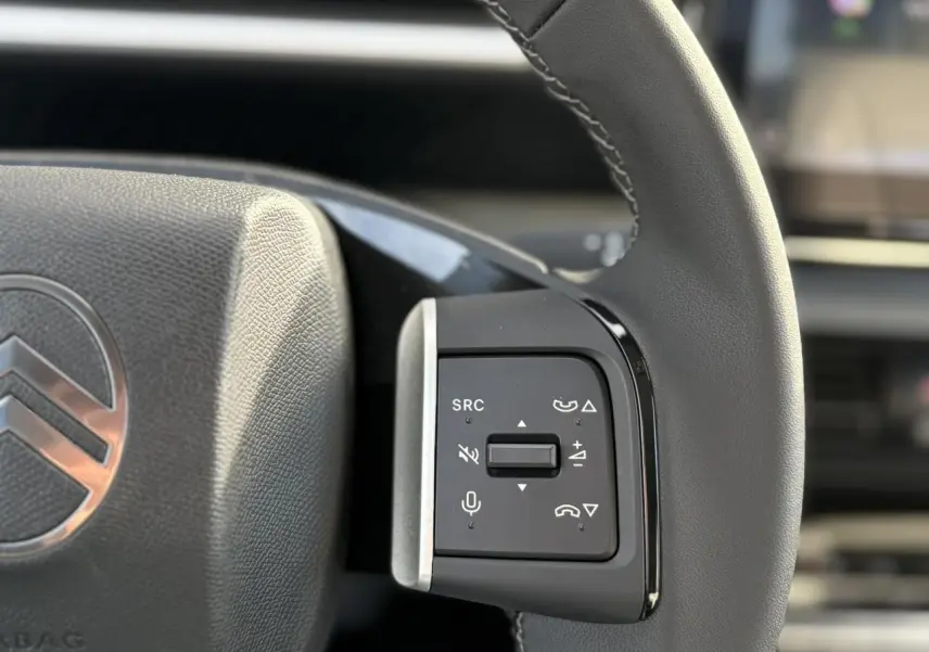 Gros plan sur les commandes multifonctions noires à droite du volant gris du Citroën C3 Aircross Hybrid 2025.