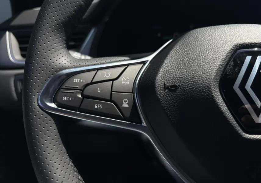 Gros plan sur le volant cuir perforé de la Renault Captur 2025, avec commandes du régulateur adaptatif côté gauche.