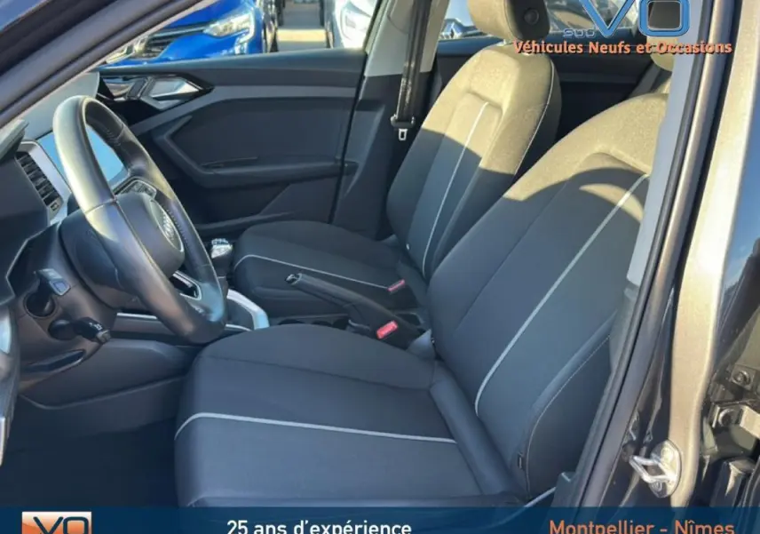 Intérieur avant de l'Audi A1 Sportback gris foncé, sièges sport noirs avec surpiqûres claires et volant cuir visible côté gauche.