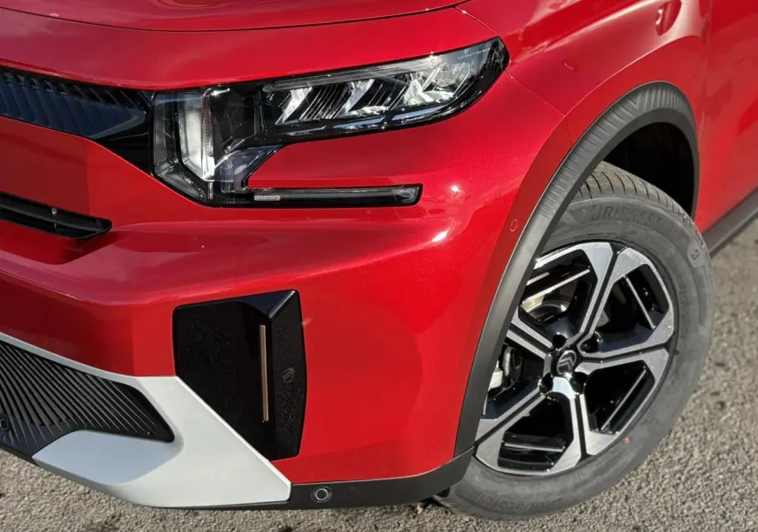 Gros plan sur l'avant droit rouge Elixir du Citroën C3 Aircross 2025, mettant en valeur le phare LED et la jante alliage noire.