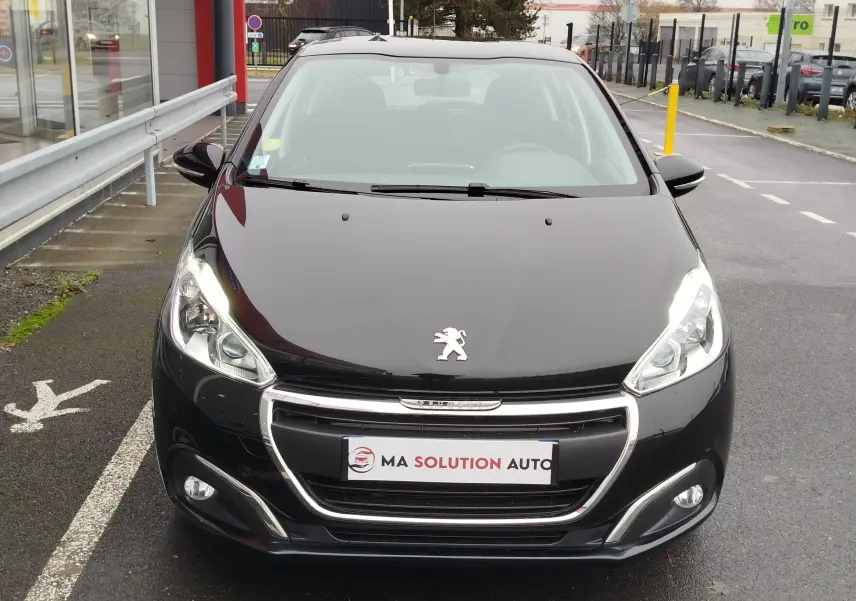 Vue avant d'une Peugeot 208 noire Perla Nera de 2019 avec phares allumés et calandre chromée visible.