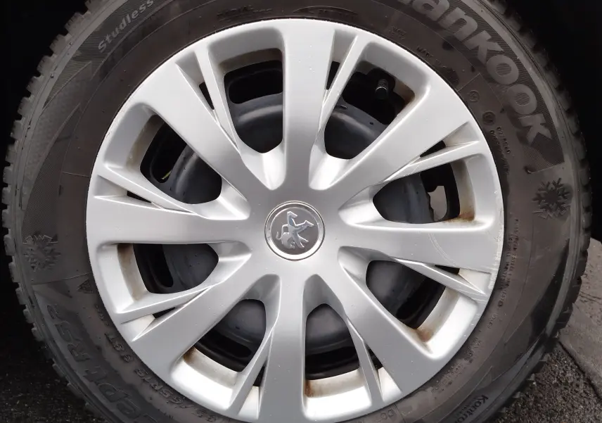 Gros plan sur la jante argentée d’une roue de Peugeot 208 noire, avec logo lion au centre et pneu hiver Hankook.