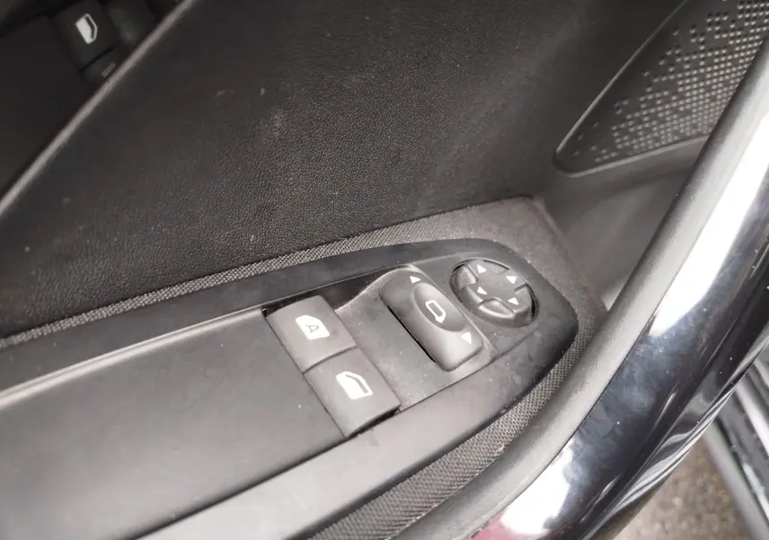 Gros plan sur les commandes de réglage des vitres et des rétroviseurs côté gauche d’une Peugeot 208 noire Perla Nera de 2019.