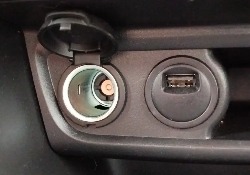 Gros plan intérieur sur la prise allume-cigare ouverte et un port USB à côté dans une Peugeot 208 noire.