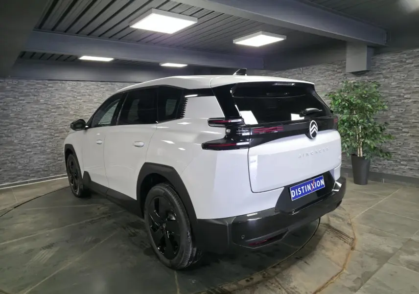 Vue 3/4 arrière droite du Citroën C5 Aircross blanc avec toit noir et jantes alliage noires en intérieur showroom.