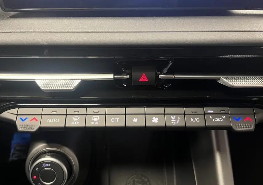 Gros plan sur la console centrale de l'Alfa Romeo Tonale gris foncé, montrant les commandes de climatisation et le bouton de warning.
