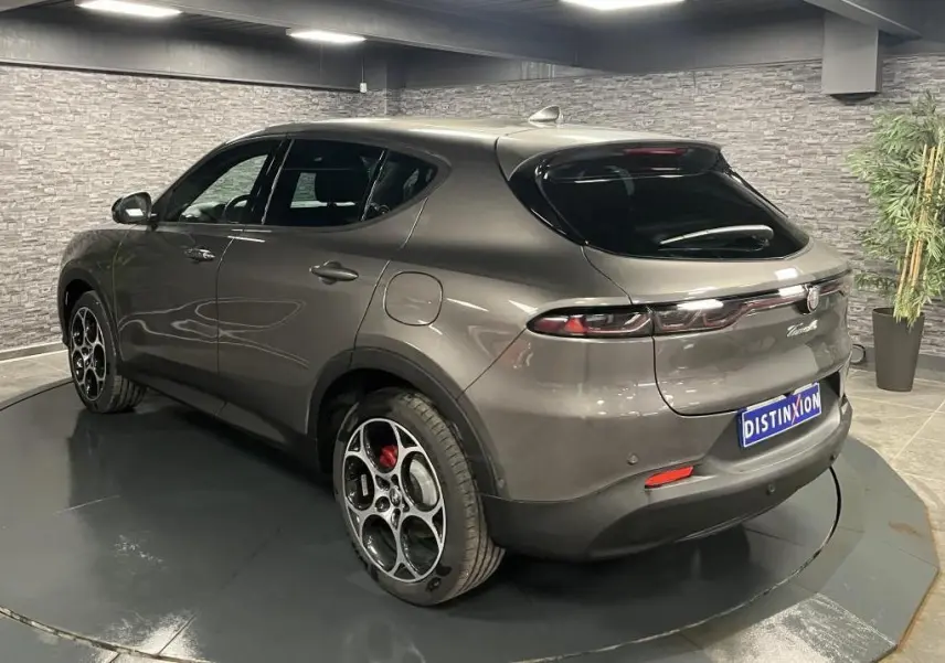 Vue 3/4 arrière droite d'une Alfa Romeo Tonale gris foncé avec jantes distinctives et feux arrière LED dans un showroom.