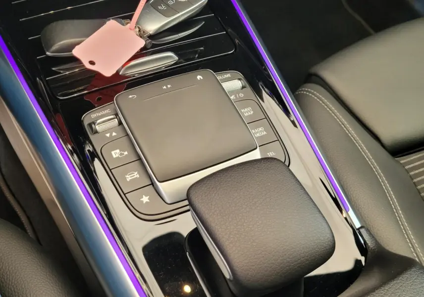 Gros plan sur la console centrale noire brillante du Mercedes GLA 200 D bleu, avec touches de commande et éclairage violet.