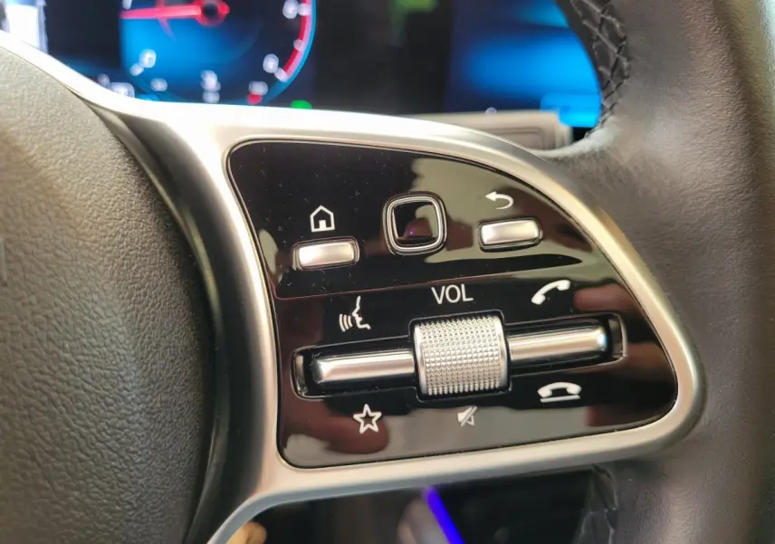 Gros plan sur les commandes de volume et fonctions vocales au volant cuir d'une Mercedes GLA 200 D bleu 2022.