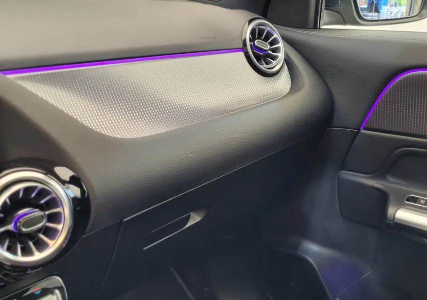 Détail intérieur côté passager du tableau de bord noir et gris avec éclairage d’ambiance violet d’une Mercedes GLA 200 D 2022.