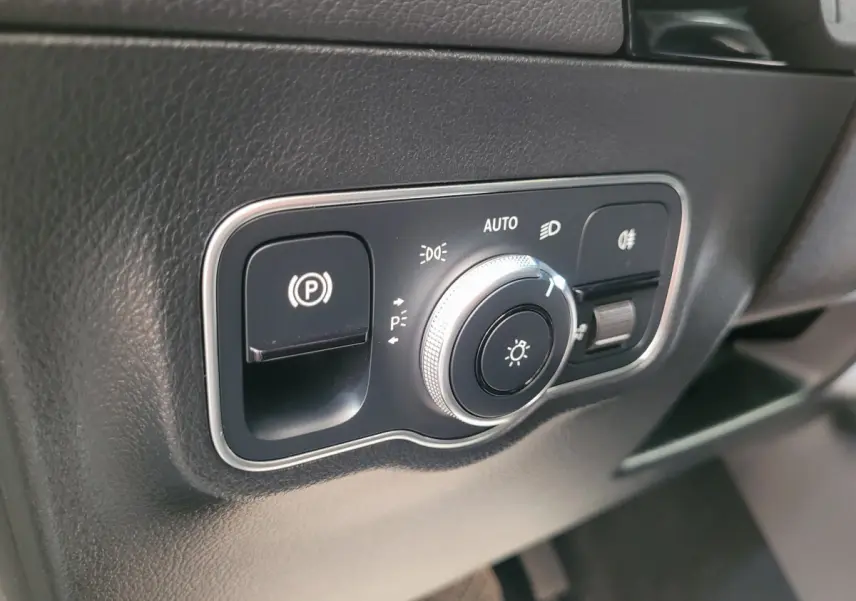 Gros plan sur le panneau de commande des phares et frein à main électrique dans une Mercedes GLA 200 D Business Line bleu 2022.