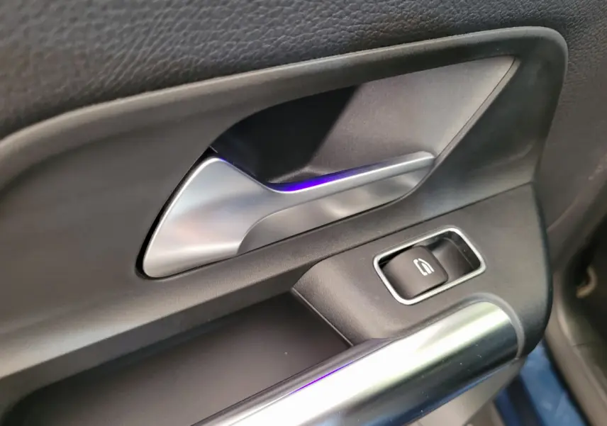 Poignée intérieure côté gauche en métal brossé avec bouton de lève-vitre sur porte d’un Mercedes GLA 200 D bleu 2022.