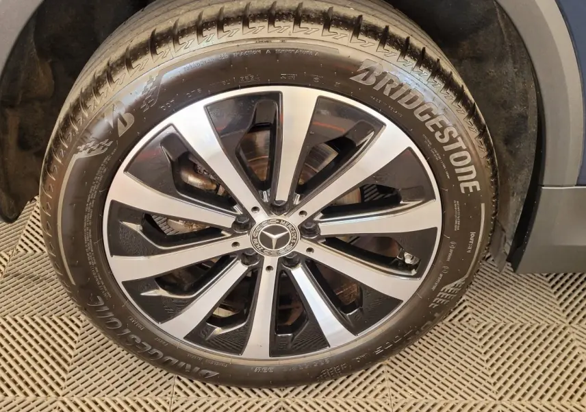 Gros plan sur la jante alliage noire et argentée avec logo Mercedes du pneu Bridgestone d’un GLA bleu 2022.