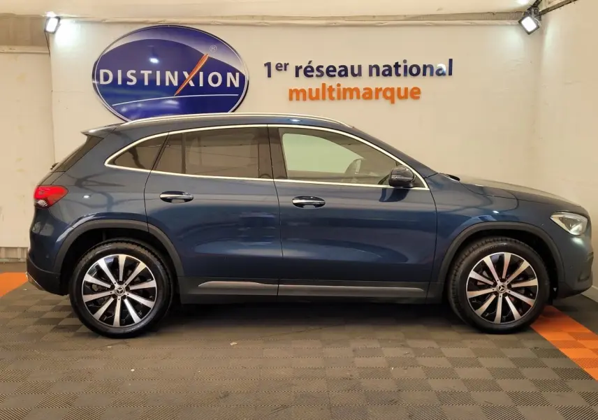 Profil latéral droit d'un Mercedes GLA 200 D Business Line bleu avec jantes alliage et toit chromé en showroom.