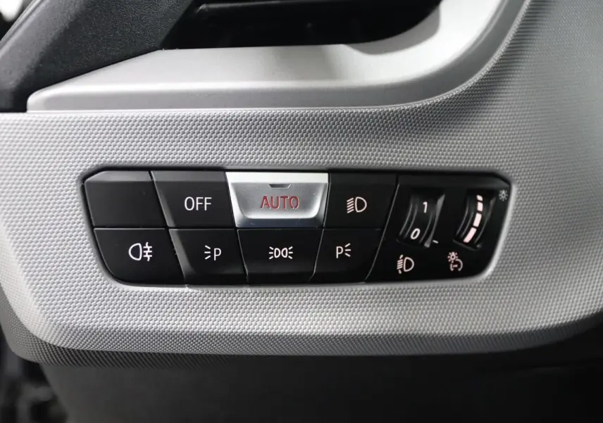 Gros plan sur les commandes d’éclairage à gauche du tableau de bord de la BMW Série 1 116d noire de 2023.