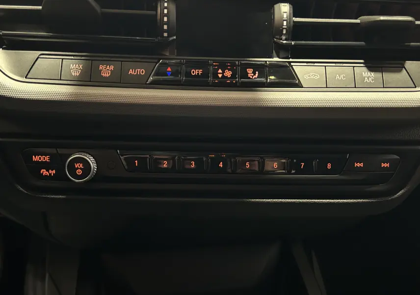 Vue rapprochée du tableau de bord noir de la BMW Série 1 116d 2023, montrant les commandes climatisation et audio rétroéclairées.