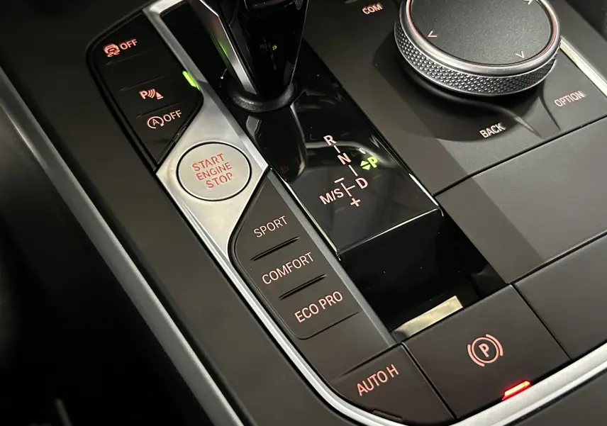 Gros plan sur la console centrale de la BMW Série 1 noire, montrant levier de vitesse automatique et boutons de modes de conduite.