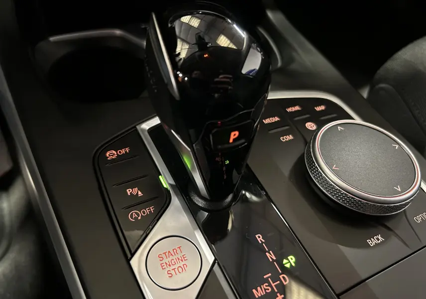 Gros plan sur la console centrale noire de la BMW Série 1 116d 2023, avec levier de vitesse automatique et bouton start/stop éclairés.