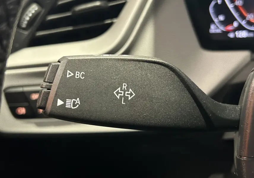 Gros plan sur la commande de clignotant noire à gauche du volant dans l’habitacle d’une BMW Série 1 noire de 2023.