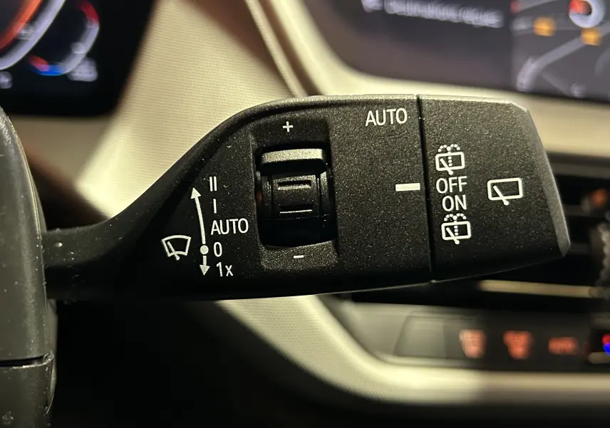 Gros plan sur la commande de l’essuie-glace à gauche du volant dans l’habitacle noir de la BMW Série 1 116d 2023.
