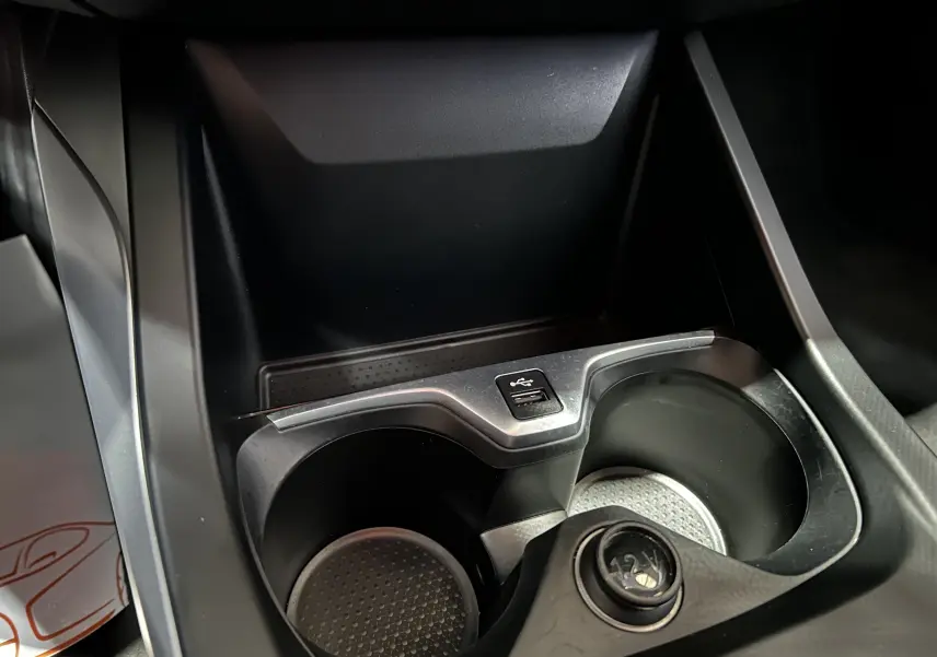 Gros plan sur la console centrale noire de la BMW Série 1 116d 2023, montrant les porte-gobelets et un port USB.