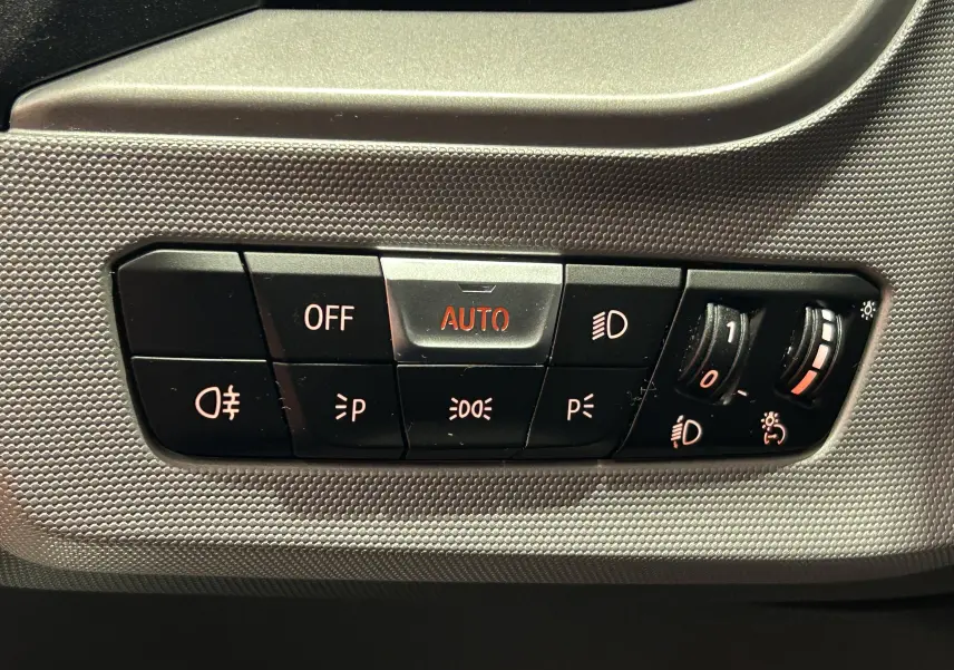 Gros plan sur les commandes d’éclairage intérieures de la BMW Série 1 noire, avec bouton AUTO en surbrillance rouge.