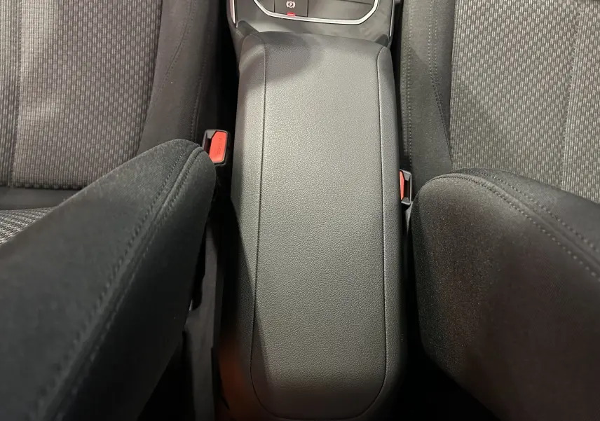 Vue plongeante sur l'accoudoir central noir entre les sièges avant en tissu gris foncé de la BMW Série 1 116d 2023.