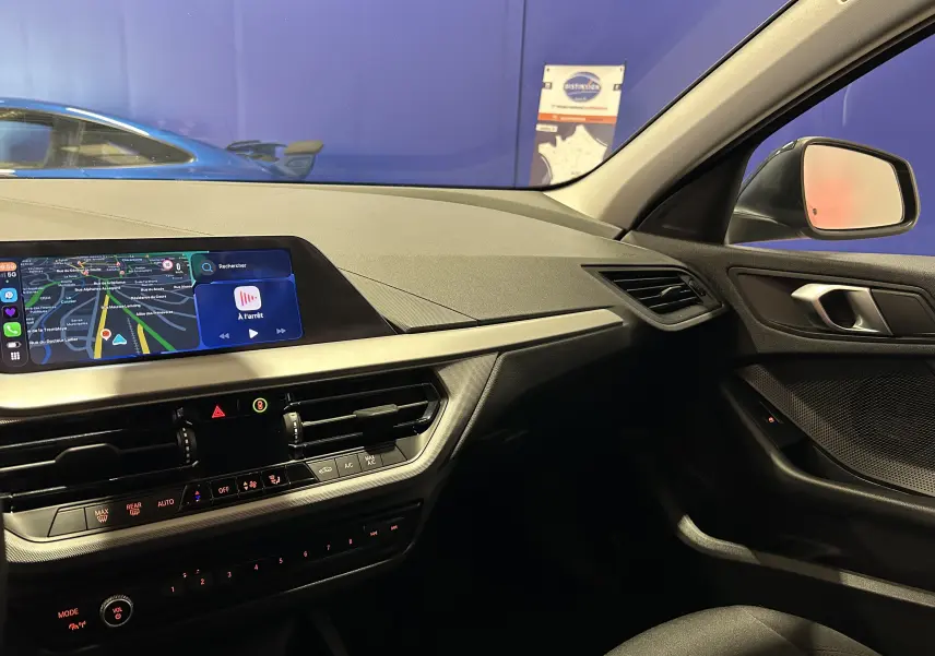 Vue intérieure côté passager de la BMW Série 1 noire 2023, avec écran GPS et tableau de bord moderne.