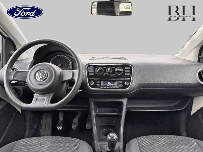 Intérieur avant d'une Volkswagen UP blanche, tableau de bord simple avec volant noir et boîte manuelle visible.