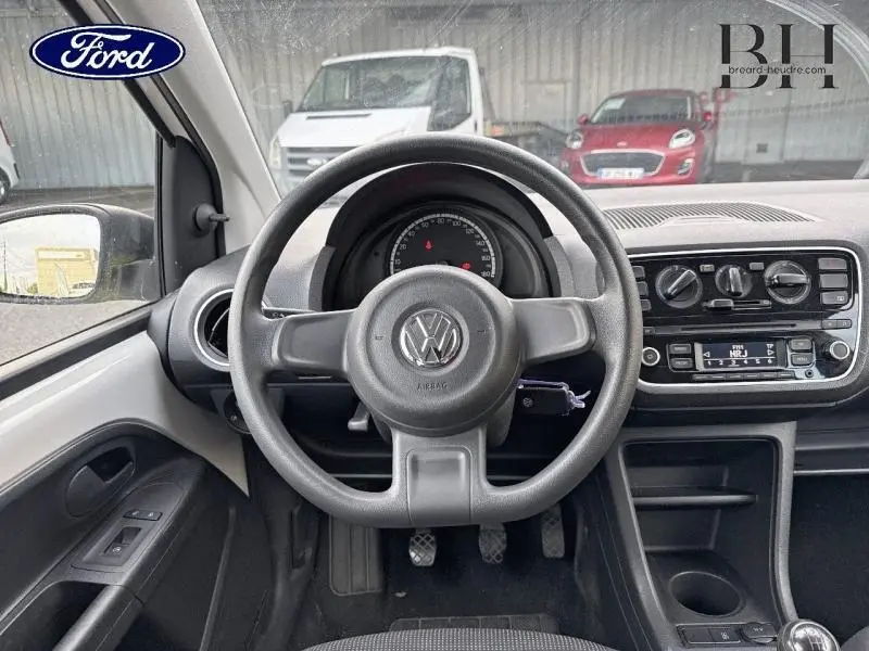 Vue intérieure centrée sur le volant Volkswagen d'une Up blanche, avec tableau de bord et commandes radio visibles.