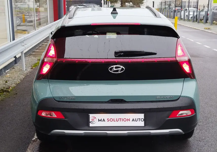 Vue arrière d'une Hyundai Bayon 2022 couleur Elemental Brass Metal avec feux allumés et hayon noir brillant.