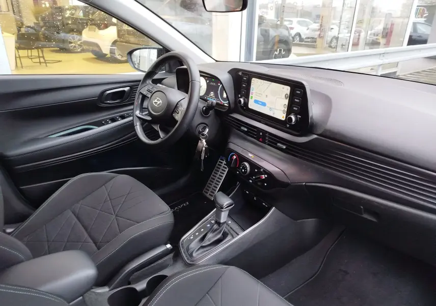 Vue intérieure côté conducteur de la Hyundai BAYON 2022, tableau de bord noir avec écran tactile et volant multifonctions.
