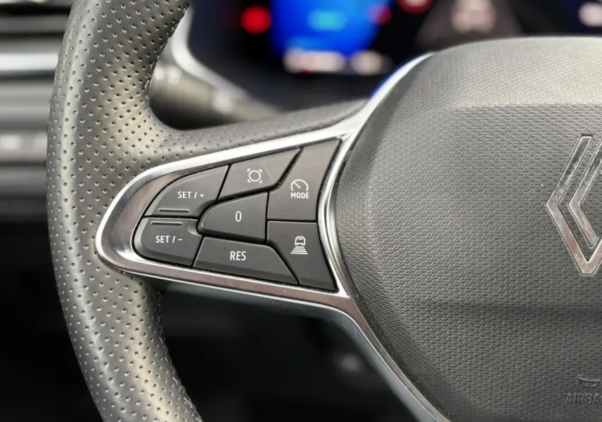 Gros plan sur la partie gauche du volant perforé du Renault Symbioz 2025, avec commandes de régulateur et logo Renault.
