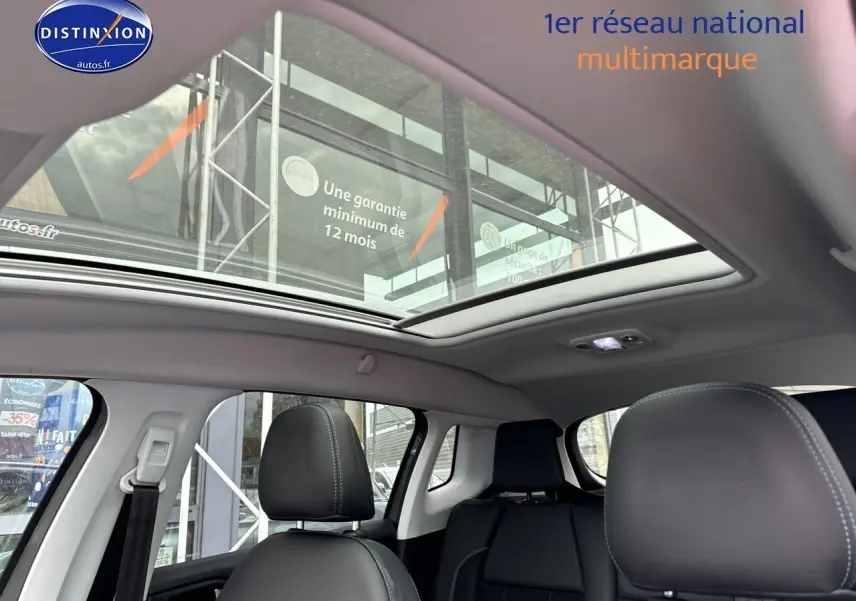 Intérieur du Peugeot 2008 gris platinium, vue sur les sièges avant et arrière avec toit panoramique ouvert.