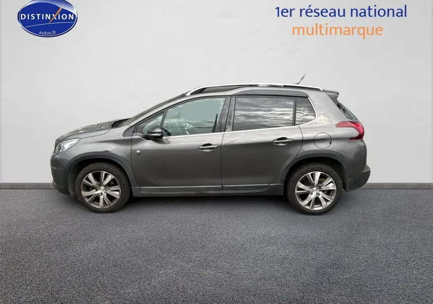 Peugeot 2008 gris platinium vue de profil côté gauche, avec jantes alliage et barres de toit visibles.