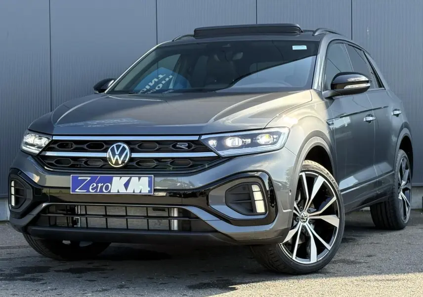 Volkswagen T-Roc gris Indium en 3/4 avant droit avec jantes alliage 19 pouces et toit ouvrant visible.