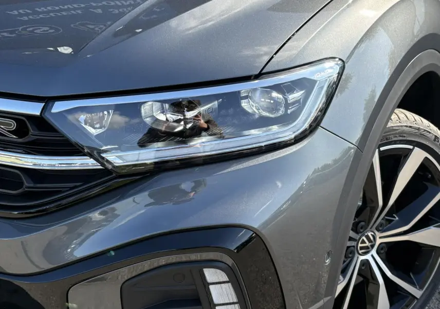 Gros plan sur l'avant droit du Volkswagen T-Roc gris Indium, mettant en valeur le phare LED et la jante alliage R-Line.