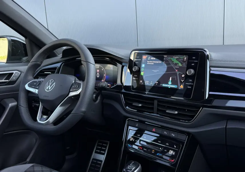 Intérieur du Volkswagen T-Roc 2025 vu côté conducteur, volant multifonction et écran tactile avec navigation affichés.