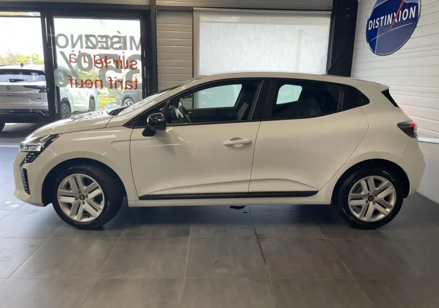 Profil côté gauche d'une Renault Clio blanche 2025 en intérieur avec jantes alliage et rétroviseurs noirs.