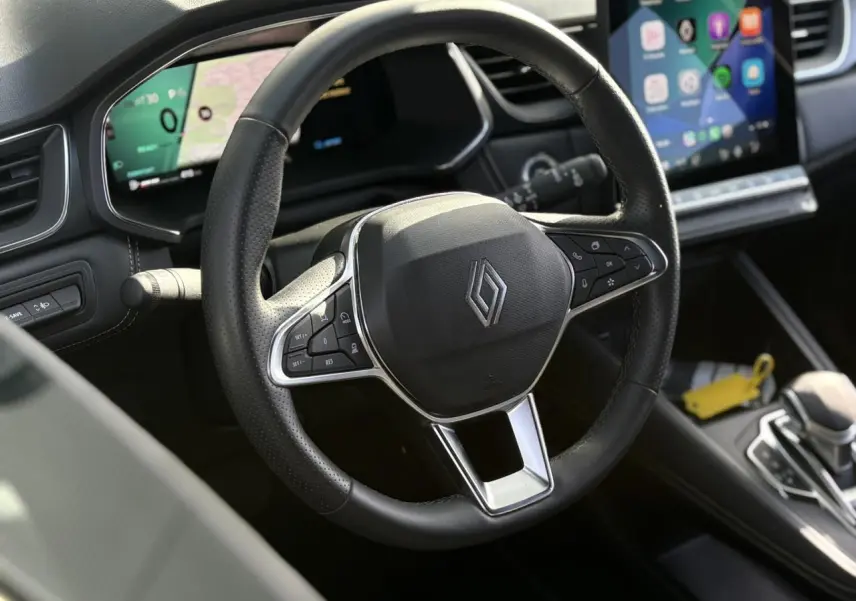 Gros plan sur le volant noir perforé du Renault Symbioz 2025 avec tableau de bord numérique et écran tactile vertical.