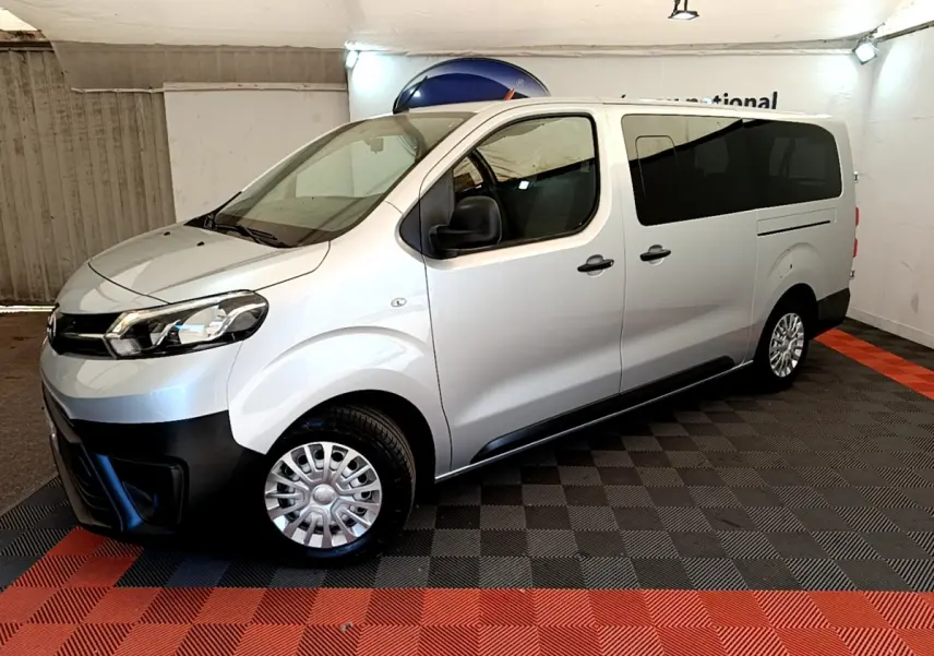 Vue côté gauche en 3/4 avant d'un Toyota Proace Verso gris clair avec vitres arrière teintées et jantes acier.