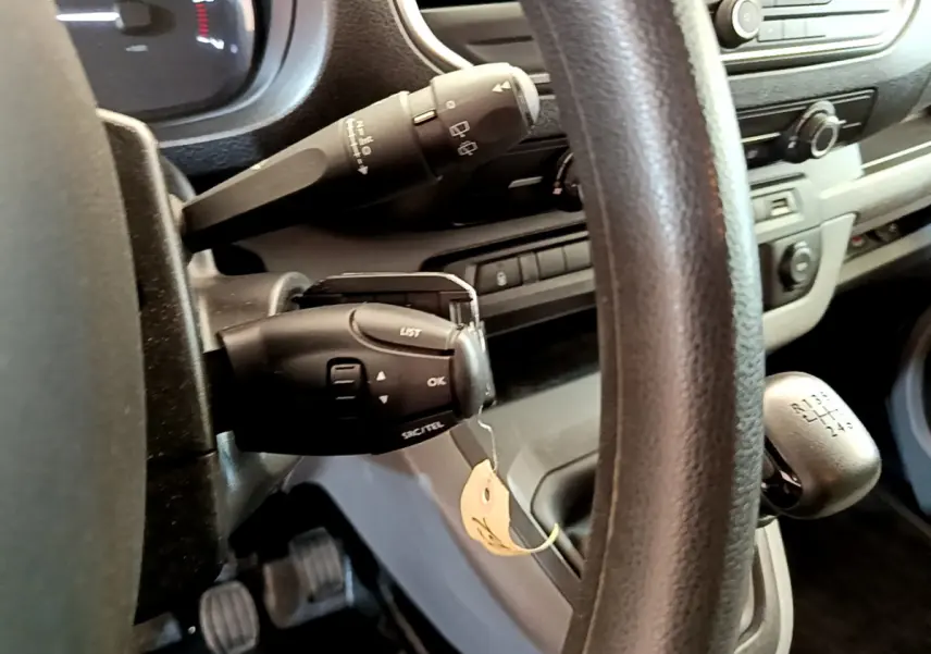 Vue rapprochée du volant noir et levier de vitesses manuel du Toyota Proace Verso gris clair, tableau de bord en arrière-plan.