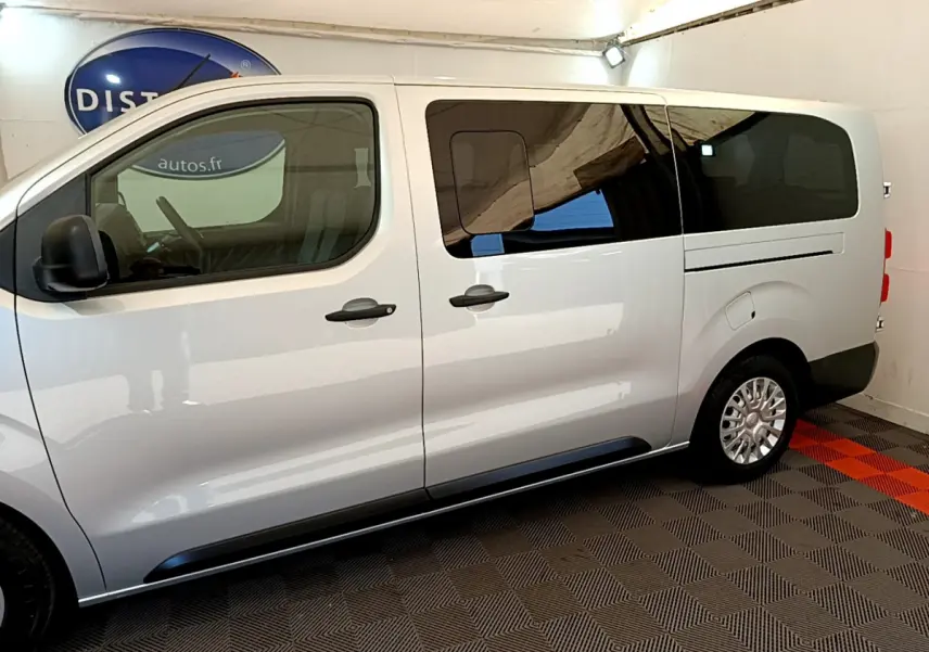 Vue latérale droite d'un Toyota Proace Verso gris clair avec vitres arrière teintées dans un intérieur fermé.