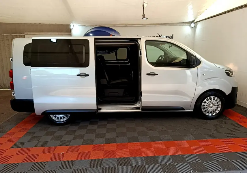 Profil droit d'un Toyota Proace Verso gris clair 2019 avec porte coulissante ouverte montrant l'intérieur sombre.