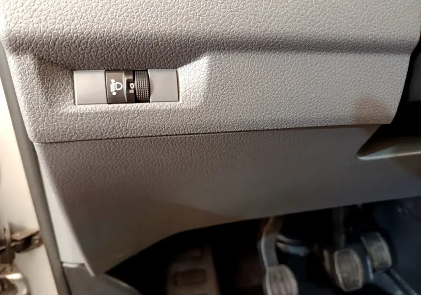 Gros plan sur le réglage manuel en hauteur des phares sous le tableau de bord gris clair du Toyota Proace Verso 2019.