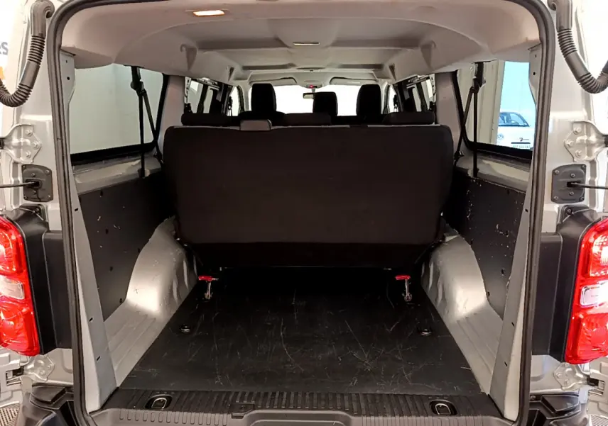 Vue arrière du coffre ouvert d'un Toyota Proace Verso gris clair, montrant la banquette arrière noire et l'espace de chargement vide.