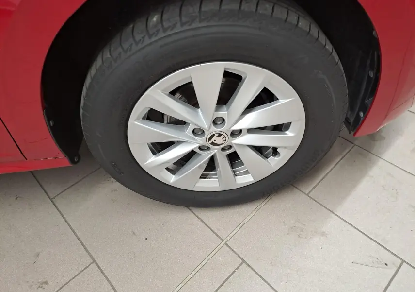 Gros plan sur la roue avant gauche d'un Skoda Kamiq rouge Velvet avec jante alliage et logo central visible.