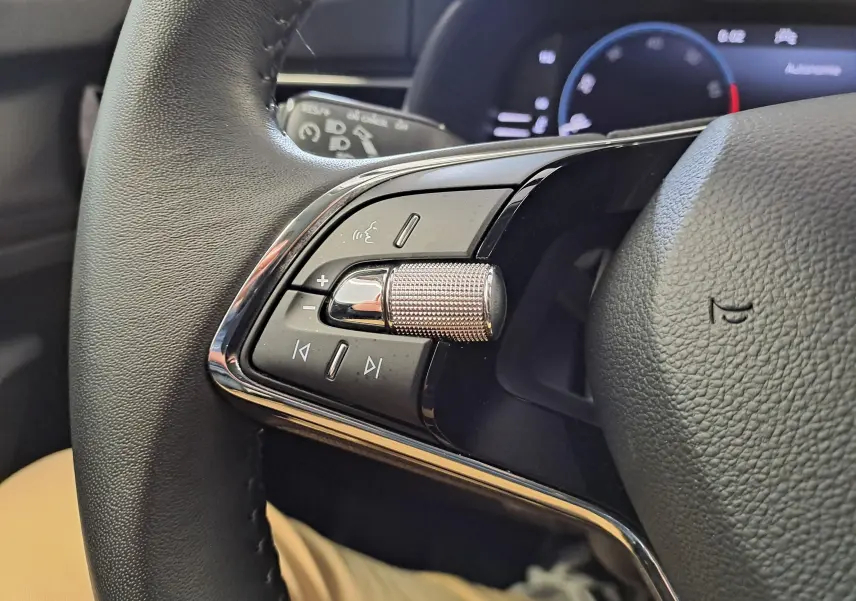 Gros plan sur les commandes du volant du Skoda Kamiq 2024, mettant en valeur la molette métallique et le cuir noir.