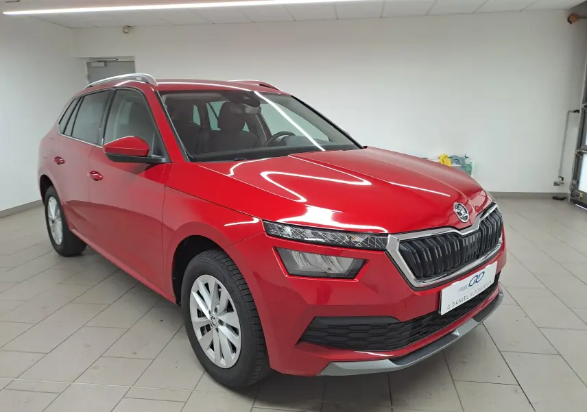 Vue 3/4 avant d'un Skoda Kamiq 2024 rouge Velvet avec calandre noire et jantes argentées en intérieur showroom.